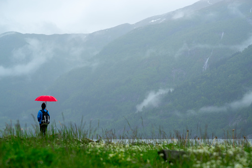 Female tourist with red umbrella on fjord shore, taking photo with camera. Tourism and traveling concept.