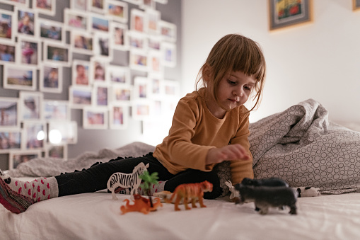 Creative young girl playing with toy animals in bed
