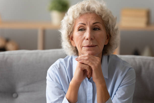 istock Head shot peaceful older woman dreaming alone, sitting on couch 1201295572