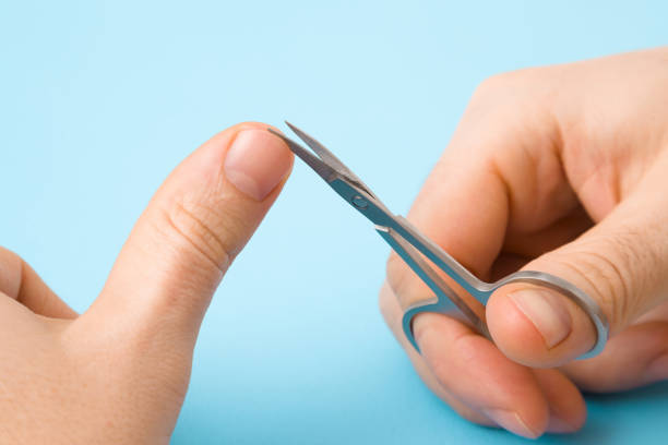 Man hand using scissors for cutting nails. Pastel blue background. Closeup. Point of view shot.