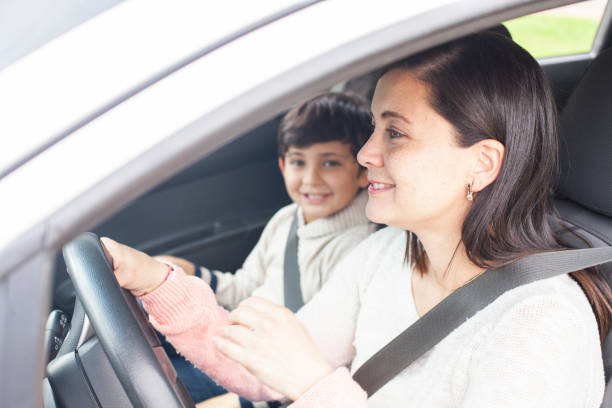 latin woman breast of approximately 35 years of brown hair drives her gray car while her 8-year-old son is sitting in the co-pilot's chair looking at the camera for the photo - 35 40 years fotos imagens e fotografias de stock