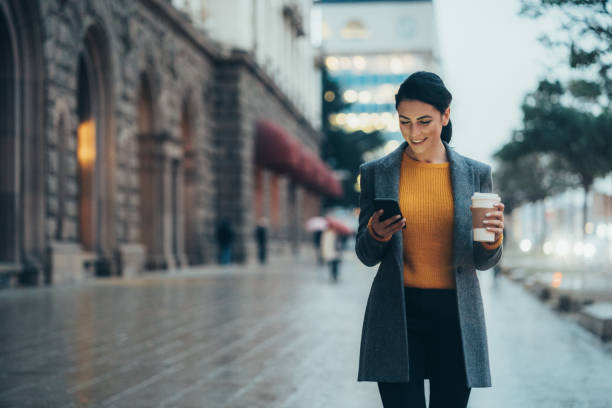 Texting in the city Modern young woman walking on the city street texting and holding cup of coffee well dressed stock pictures, royalty-free photos & images