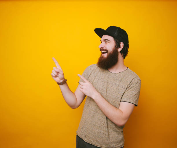 istock Smiling bearded man poiting and looking at left, copy space, over yellow background 1201300570