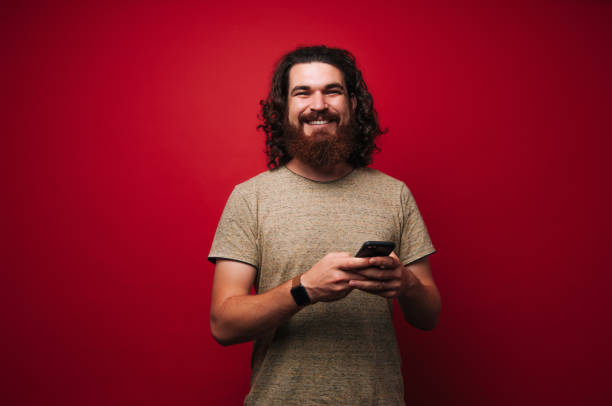 istock Smiliing bearded man with long hair, using phone and looking at camera 1201300852