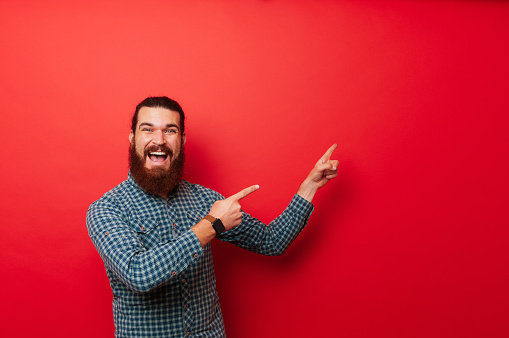 Studio photo of bearded man in glasses pointing to right and being excited