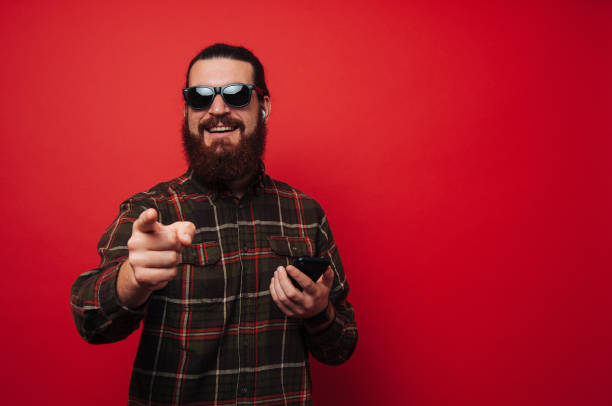 istock Happy smiling bearded hipster, using phone and gesturiing and looking at camera 1201301596