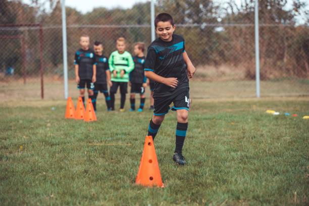 istock Young player in soccer jersey running between cones and ring ladder marker 1201303328