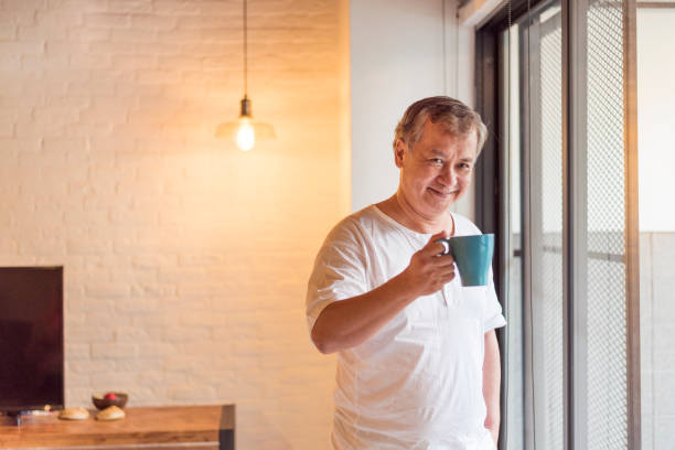 istock Senior Asian man standing by the window holding coffee cup 1201303773