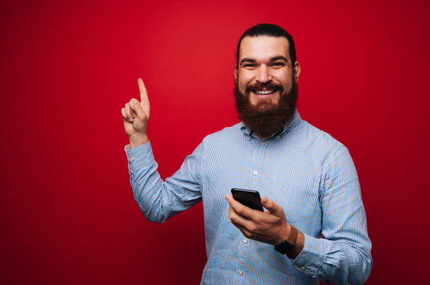 istock Happy smiling bearded man in tshirt holding a mobile and pointing up 1201303823