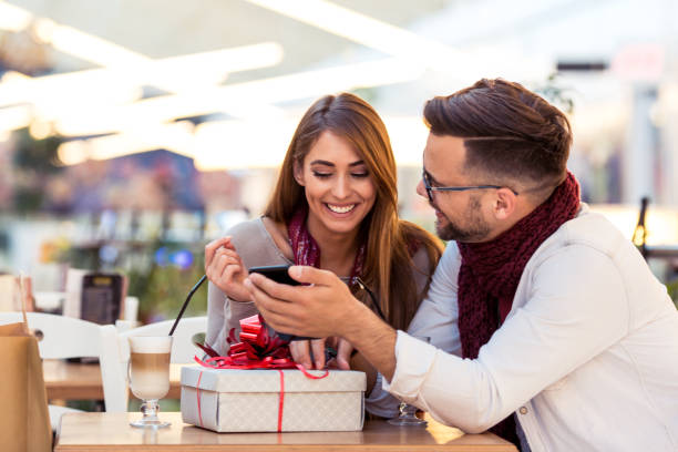 쇼핑몰에서 선물과 스마트 폰 을 들고 이야기하는 커플. 그들은 앉아서 커피를 마시고 있습니다. - gift ribbon straight wrapped 뉴스 사진 이미지