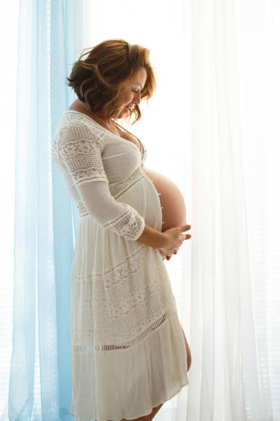 istock Pregnant woman standing by the window 1201320078
