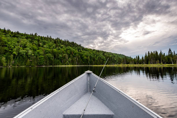 A fishing rod in a boat on a lake and forest in background in Lanaudiere area, Quebec during the fishing season.
