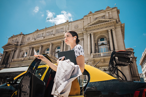 Mid adult attractive Hispanic businesswoman getting out of taxi in the city