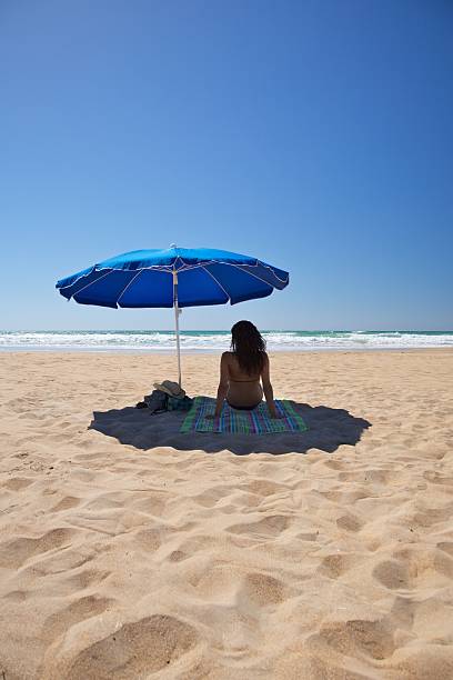 femme assis sur la serviette bleue sous le parasol de plage vacances d'été - cadiz andalusia beach spain photos et images de collection