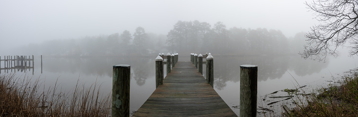 Panorama view of a wooden pier in a dense morning fog.