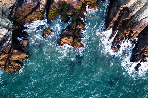 Aerial drone views looking straight down from above rugged Rocky coasts along San Francisco California Pacific coast highway landscape , blue Pacific ocean waves crashing along jagged rocks