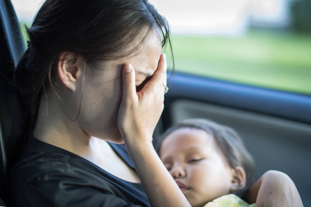 Stressed tired mother suffering from postpartum depression, holding her baby. A parent covering her face, exhausted from taking care of her baby. Resting in the car. worried mom with kids stock pictures, royalty-free photos & images
