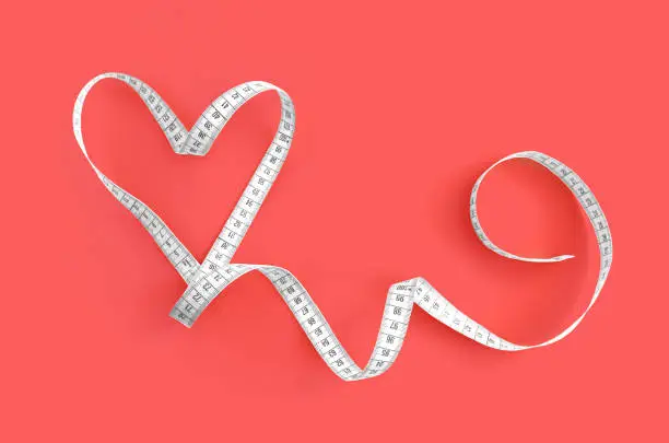 Heart made of white measuring tape isolated on a pink background. Valentine's Day Concept. Healthy lifestyle concept.