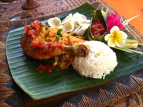 Roasted chicken leg in tomato sauce with herbs and served on a banana leaf \n Indonesian cuisine