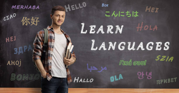 istock Male student with books standing in front of a blackboard with text learn languages 1201368027