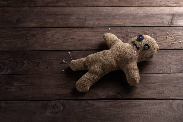 Voodoo doll on a wooden background with dramatic lighting. The concept of witchcraft and black art. Burlap doll on a wooden background. Pierce with maces. Copy space. stock photo