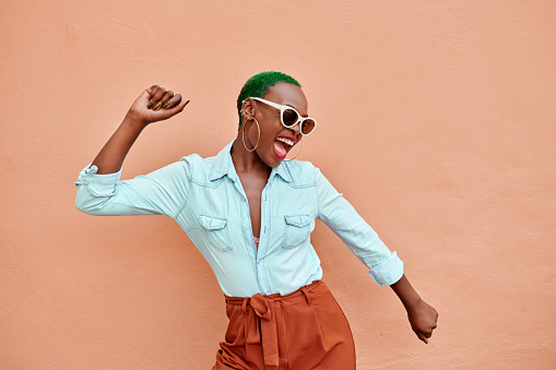 Cropped shot of a cheerful young woman dancing against a orange background outside during the day