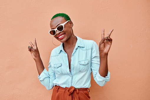 Portrait of a cheerful young woman posing while showing the peace sign against a orange background
