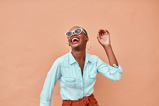 Cropped shot of a cheerful young woman dancing against a orange background outside during the day