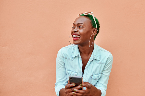 Cropped shot of an attractive young woman texting on her cellphone while standing against a orange background