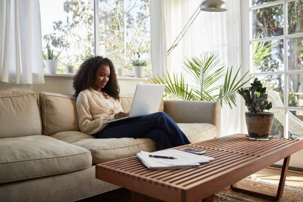 istock Smiling woman sitting on a sofa at home using a laptop 1201381043