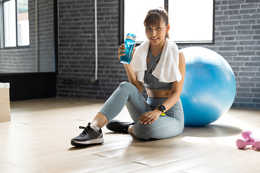 Young woman asian drink water after workout In a room with a window with natural light. Fitness and healthy lifestyle concept