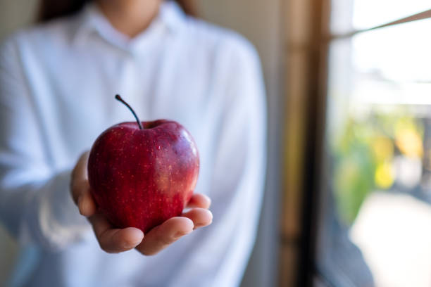istock a woman holding and giving a red apple 1201385378