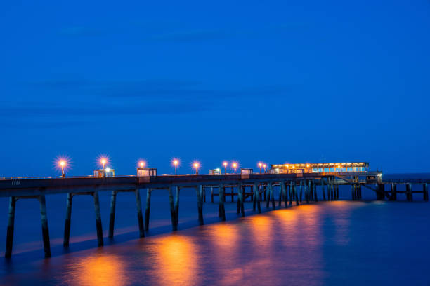 cais de negócios à noite iluminado por luzes refletidas na água abaixo. - deal kent - fotografias e filmes do acervo