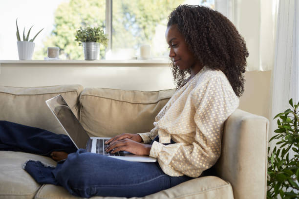 istock Smiling young woman using a laptop while relaxing on her sofa 1201390520