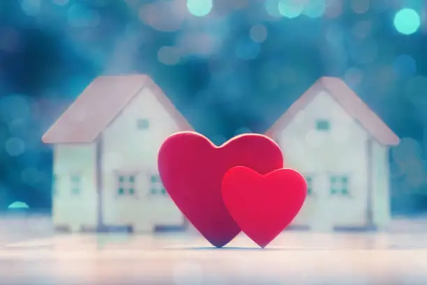 Photo of Two hearts and house models over defocused lights. Valentine's day concept