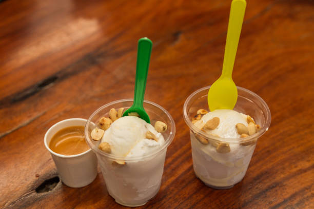 Two small cups filled with ice cream made of coconut milk and topped with hole peanuts. Plastic bowls and spoons for the ice cream. Served together with av nice strong espresso.