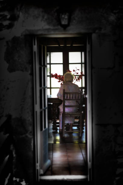 old lady seen from behind and seen through the door of the house, sitting in her house