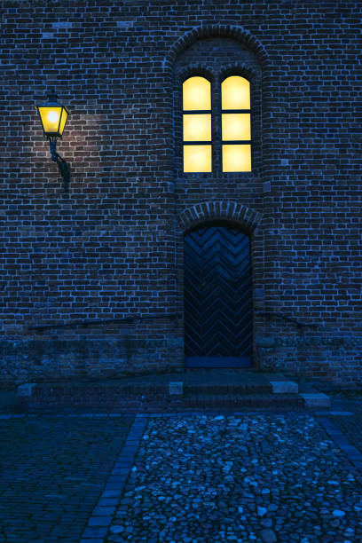 istock Old church with illuminated window and lantern at dusk. 1201404237