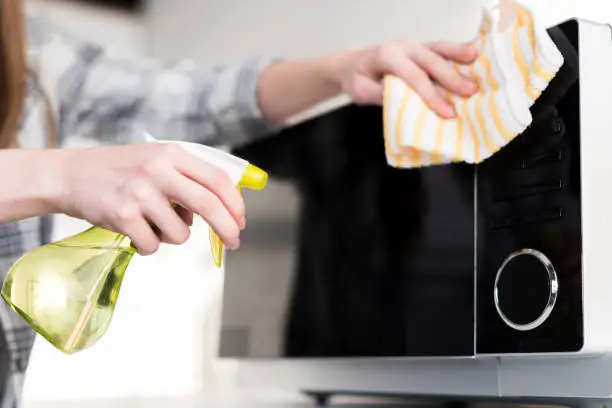 Photo of cropped view of woman cleaning microwave with rag in kitchen