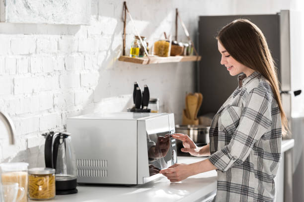side view of smiling woman in shirt using microwave in kitchen side view of smiling woman in shirt using microwave in kitchen inside microwave stock pictures, royalty-free photos & images