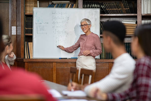 Teacher explaining maths to university class Senior teacher explaining math formulas written on whiteboard in library while college students sitting on table understanding the concept. Happy mature woman lecturer clearing doubts to students in class. Professor teaching to high school guys and girls. interrogation woman stock pictures, royalty-free photos & images