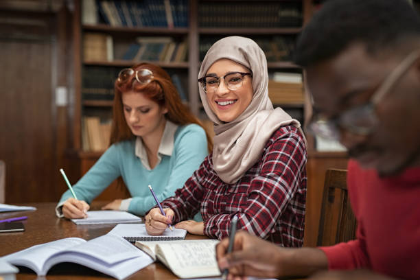 Islamic student at library Happy young woman in hijab at university library looking at camera. Portrait of smiling female student wearing abaya and spectacles feeling confident. Islamic girl studying with multiethnic students. veil photos stock pictures, royalty-free photos & images
