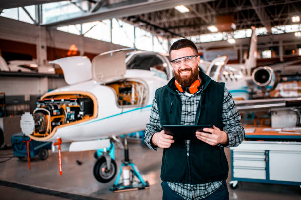 istock Aircraft engineer smiling and looking at a camera while holding a digital tablet and repairing and maintaining an airplane 1201407322