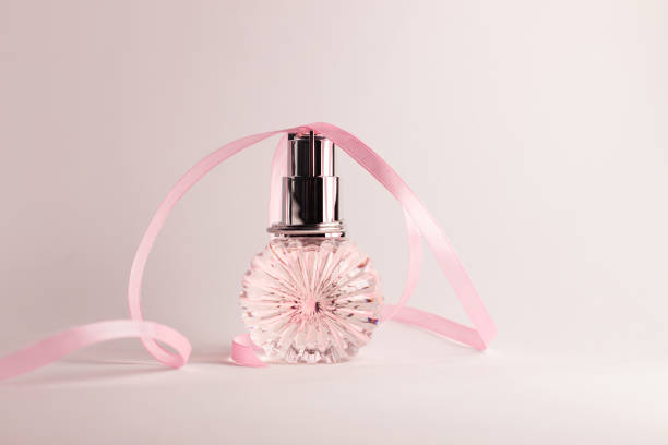 Creative perfume bottle with cute pink ribbon on light background. Blank perfumery mockup, spa branding concept.Glamour fragrance,Eau de parfum.Holiday gift banner.Luxury beauty cosmetics brand design