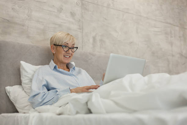 istock Senior woman using laptop in bed 1201411234