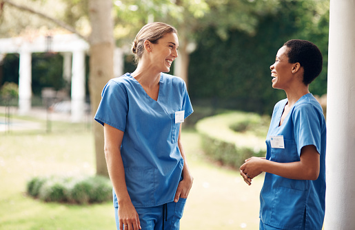 Shot of two young nurses talking outside in the garden of a retirement home