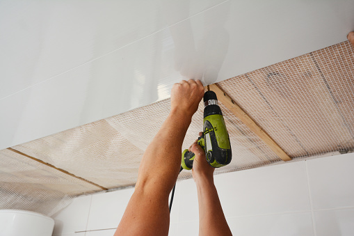 Contractor installing, renovate, repair white PVC Ceiling Boards with screw gun in the new room