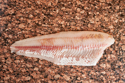 Fresh raw pike perch fish fillet on marble dark brown table. Top view, close up