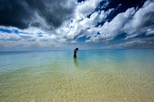 Silhouette of a woman in a bikini showcasing mystical clear blue water, smoky clouds and approaching storm.