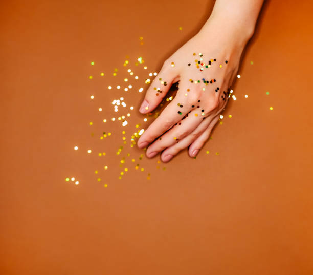 istock Woman's hand and golden glitters on warm brown background. 1201416347